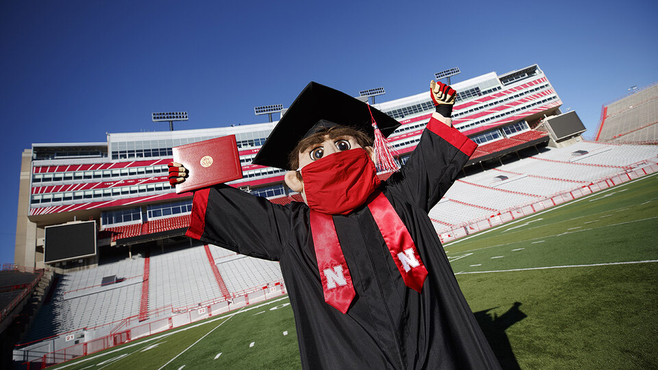 Herbie Husker wears a cap and gown on the field in Memorial Stadium.